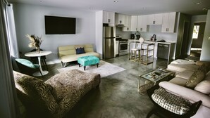 Un salon moderne comprenant un canapé, un pouf, une table basse et un coin repas avec une table et des chaises.