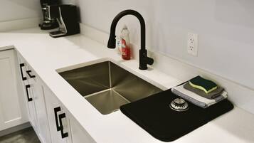 A kitchen with a stainless steel sink, a coffee maker, and a bottle of dish soap.
