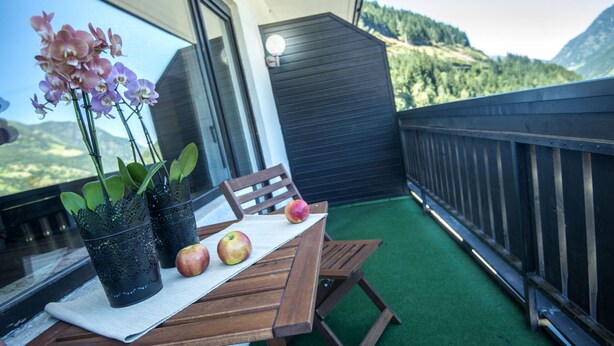 Een balkon met een houten tafel, twee potorkideeën en twee appels.