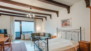Ein Schlafzimmer mit Bett, Schreibtisch, Sessel, Sofa, Nachttisch und einem Fenster mit Vorhängen.