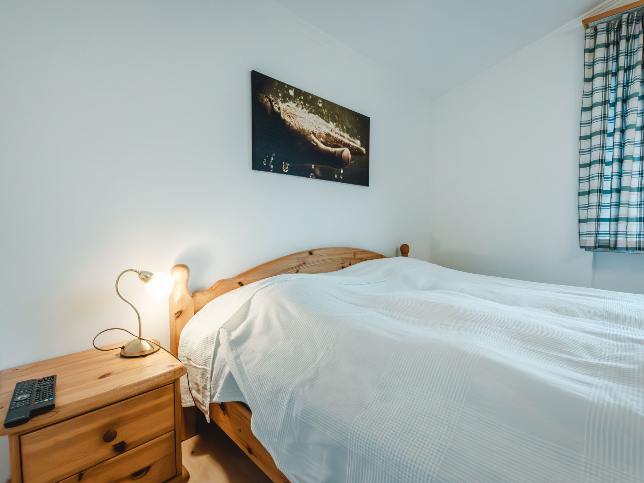 A bedroom with a wooden bed, a bedside table with a lamp, and a painting on the wall.
