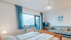 A hotel room with two beds, a television, a sofa, and a large window with a view of buildings and mountains. - Landhaus St. Georg by Interhome (Bad Gastein)