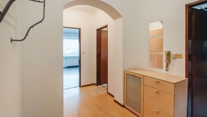 Un pasillo con piso de madera, una puerta que da a otra habitación y un mueble pequeño con cajones.