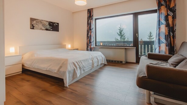 Et soveværelse med seng, natbord, kommode, et vindue med udsigt og en sofa.