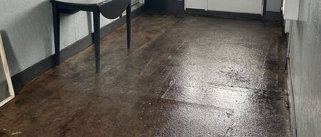 A room with a polished concrete floor, a dark wooden table, a mirror, and a door with a sign above it.