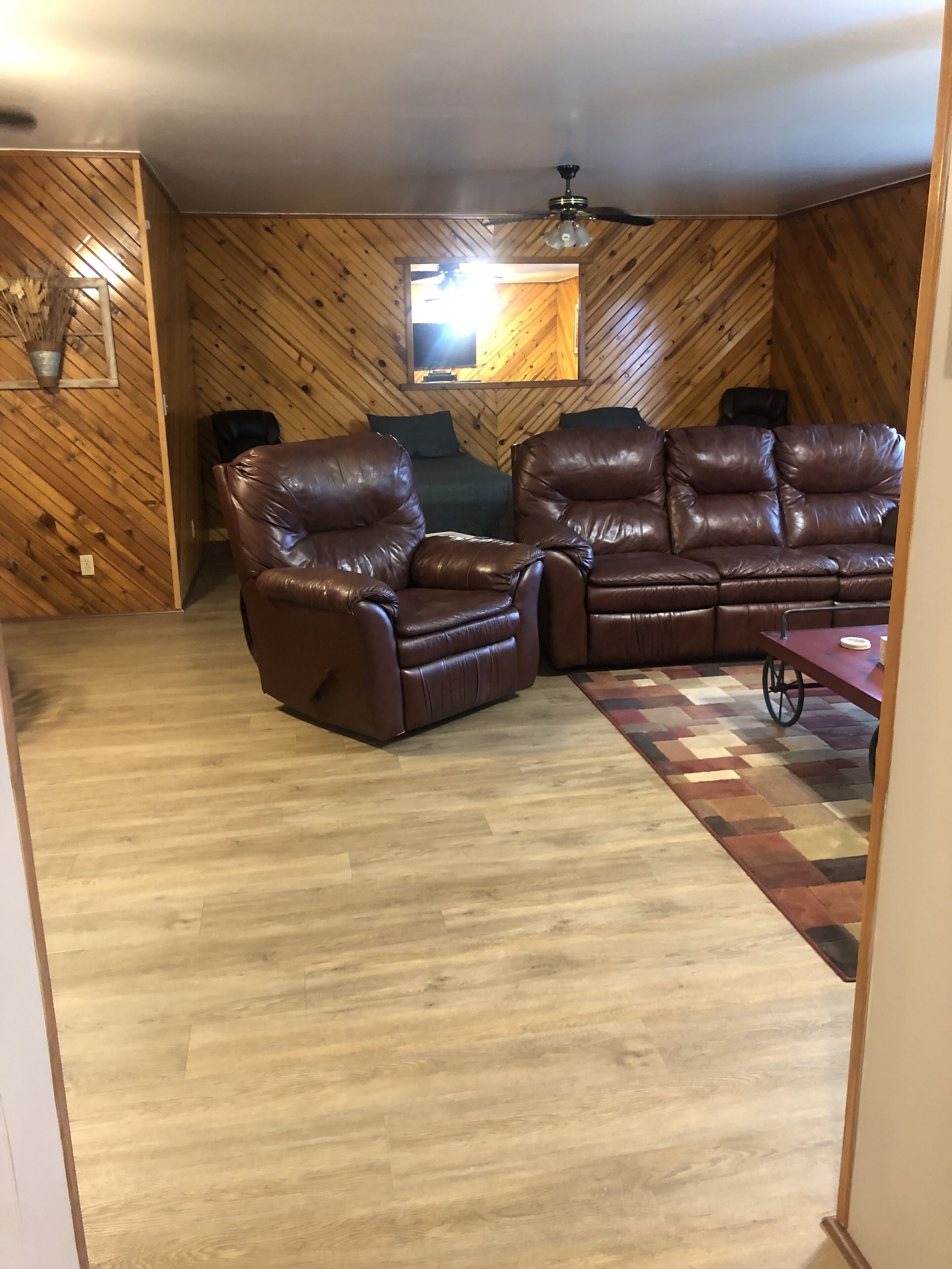 Ein Wohnzimmer mit braunem Ledersofa, einem Ledersessel und einer Wand mit Holzvertäfelung in Fischgrätmuster.