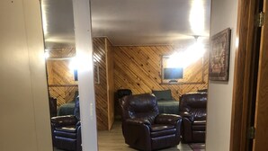 Un pasillo con piso de madera que conduce a una habitación con dos sofás de cuero y un televisor instalado en la pared.