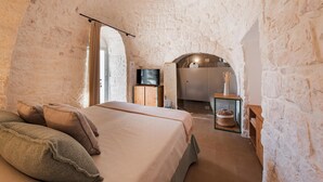 A bedroom with a large bed, a television, and a stone wall.
