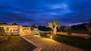 A well-lit outdoor area with a swimming pool, stone walls, and a covered seating area.