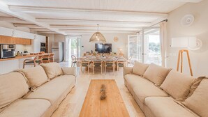 A spacious living room with a large sofa set, a wooden coffee table, and a dining area with a TV and table set.