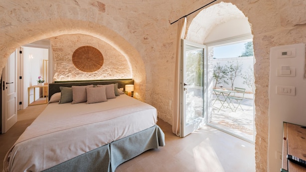 A bedroom with a stone wall, a bed with pillows, a nightstand, and a view of the outside patio.