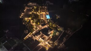 An aerial view of a well-lit resort with a swimming pool, landscaped gardens, and multiple buildings.