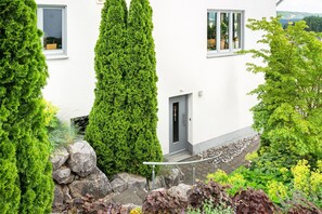 Un edificio blanco con puerta y ventanas, rodeado de vegetación y un camino de piedra.