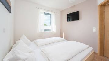 Ein Schlafzimmer mit zwei Betten, einem Fenster mit Vorhängen, einem Flachbildfernseher an der Wand und einer Holztür.