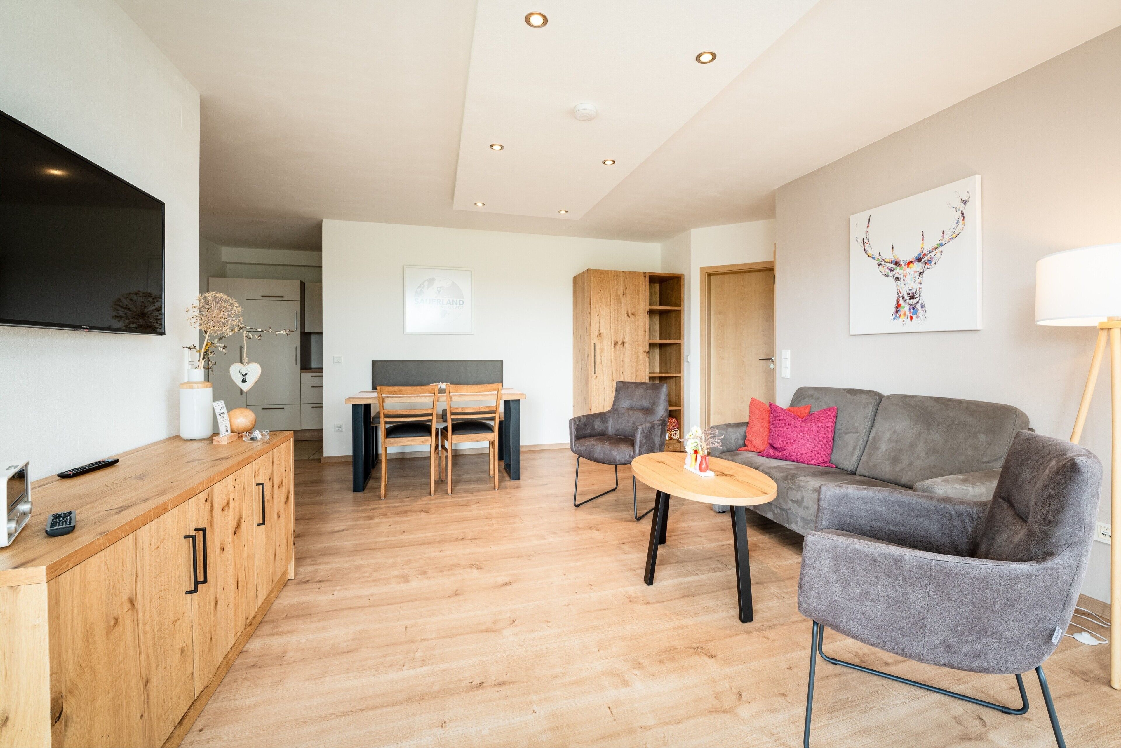 Un salon moderne avec un canapé gris, une table basse en bois et un téléviseur fixé au mur.