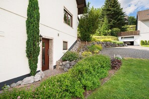 Ein weißes Gebäude mit einer Steinstufe, einer Garage und einem gepflegten Garten mit verschiedenen Pflanzen und Blumen.