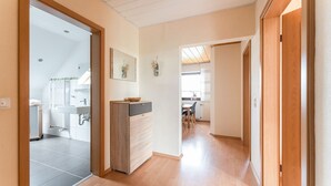A hallway with a wooden floor, a kitchen area with a sink and cabinets, and a dining area with chairs and a table.