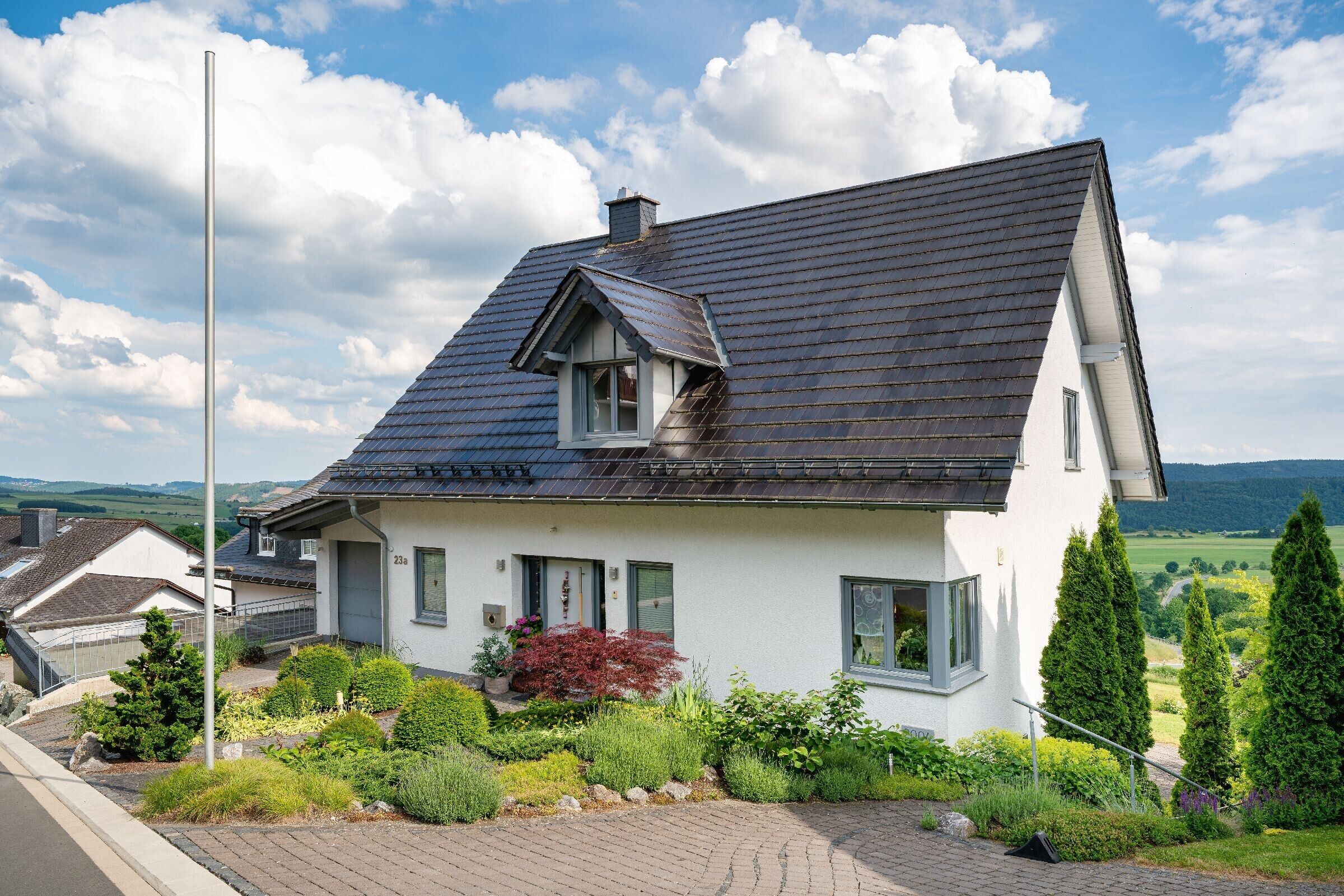 A house with a steep roof, a chimney, and a garden with various plants.
