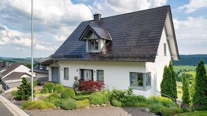 A house with a steep roof, a chimney, and a garden with various plants.