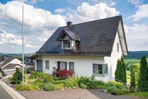 A house with a steep roof, a chimney, and a garden with various plants. - Appartement Fernblick, 55qm, Balcony (Medebach)