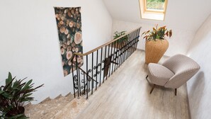 A staircase with a metal railing, a woven chair, a potted plant, and a wall-mounted tapestry.