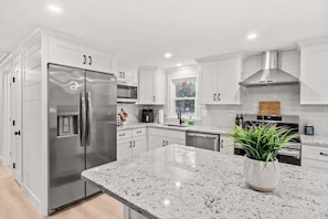 Una cocina moderna con muebles blancos, electrodomésticos de acero inoxidable y encimera de granito.