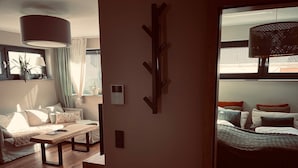 Una sala de estar moderna con un sofá, una mesa de centro y una mesa de comedor. Hay una ventana con cortinas y una planta en el alféizar.