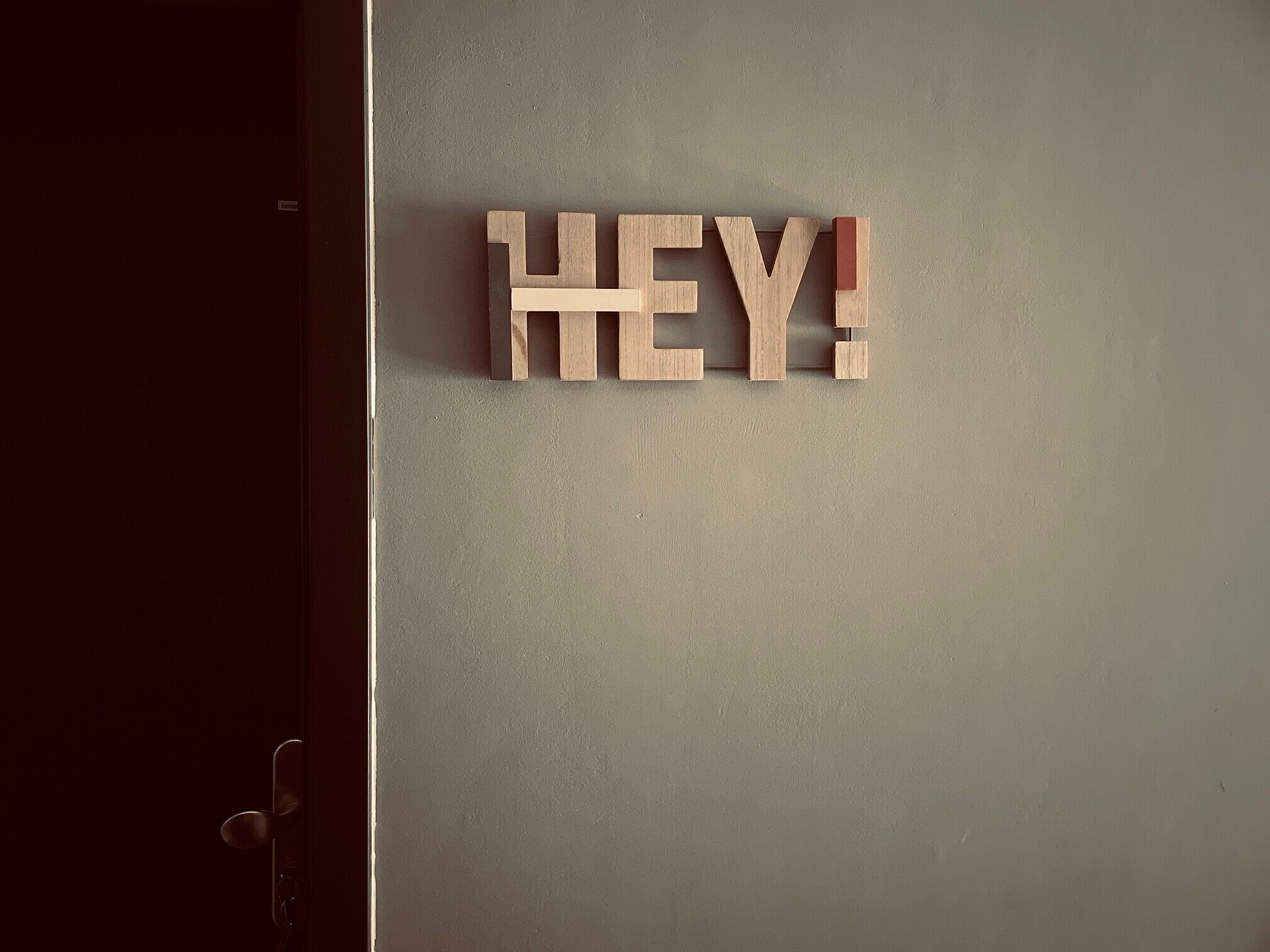 Une enseigne en bois sur laquelle est écrit le mot « HEY ! » et qui est fixée à un mur uni.