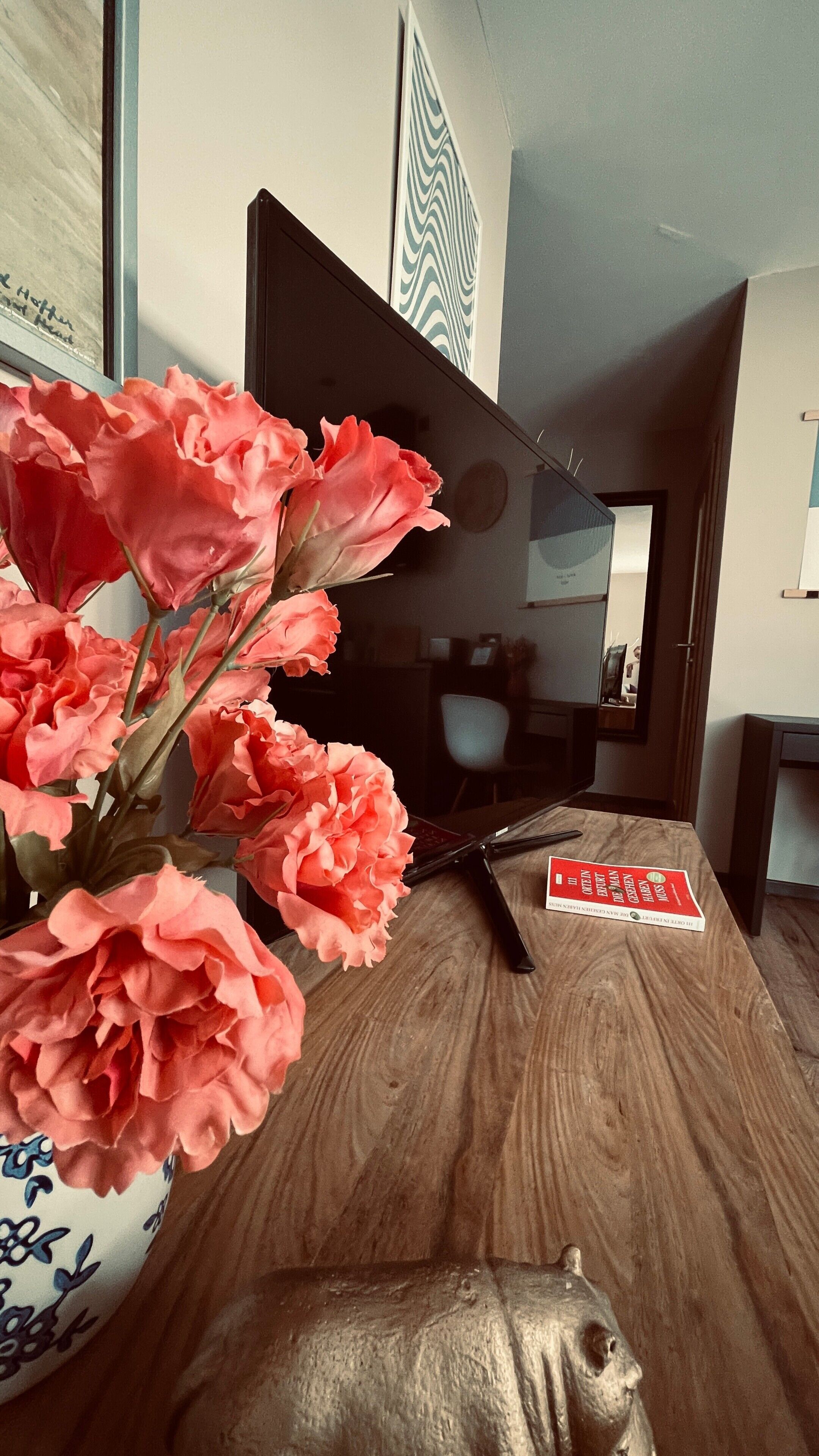 Un tavolo in legno con un vaso di fiori rosa, un telecomando e un libro.