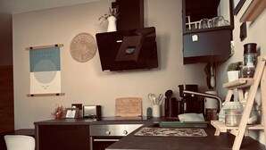 Una cocina moderna con horno integrado, cafetera y un pequeño comedor con una silla blanca.