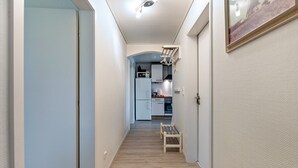 Un couloir étroit avec un banc en bois, un coin cuisine à l’arrière-plan et un tableau encadré au mur.