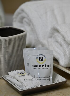 Uma bandeja com produtos de higiene pessoal, incluindo uma xícara de café, um frasco de shampoo Mancini B&B Apartments e um sabonete.