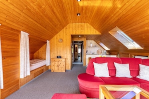 Ein gemütliches Dachzimmer mit rotem Sofa, Holzwänden, einer kleinen Küchenzeile und Dachfenstern.