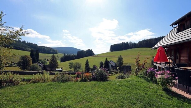 Un paysage rural avec un chalet en bois, un parapluie rouge et un champ d’herbe.