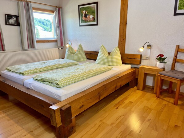 Un lit en bois avec une literie à carreaux, une table de chevet avec une lampe, une chaise et un tableau encadré au mur.