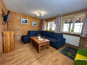 Ein Zimmer mit Holzwandverkleidung, einer dunkelblauen Couch, einem Holztisch und einem Heizkörper.