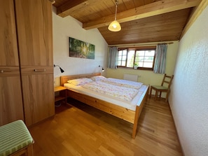 Ein Schlafzimmer mit einem hölzernen Bett, einem Schreibtisch, einem Stuhl, einem Heizkörper und einem Fenster mit Vorhängen.