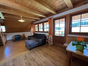 Ein Holzinterieur mit einer Couch, einem Holztisch mit einer Blume und einem Fenster mit Vorhängen.