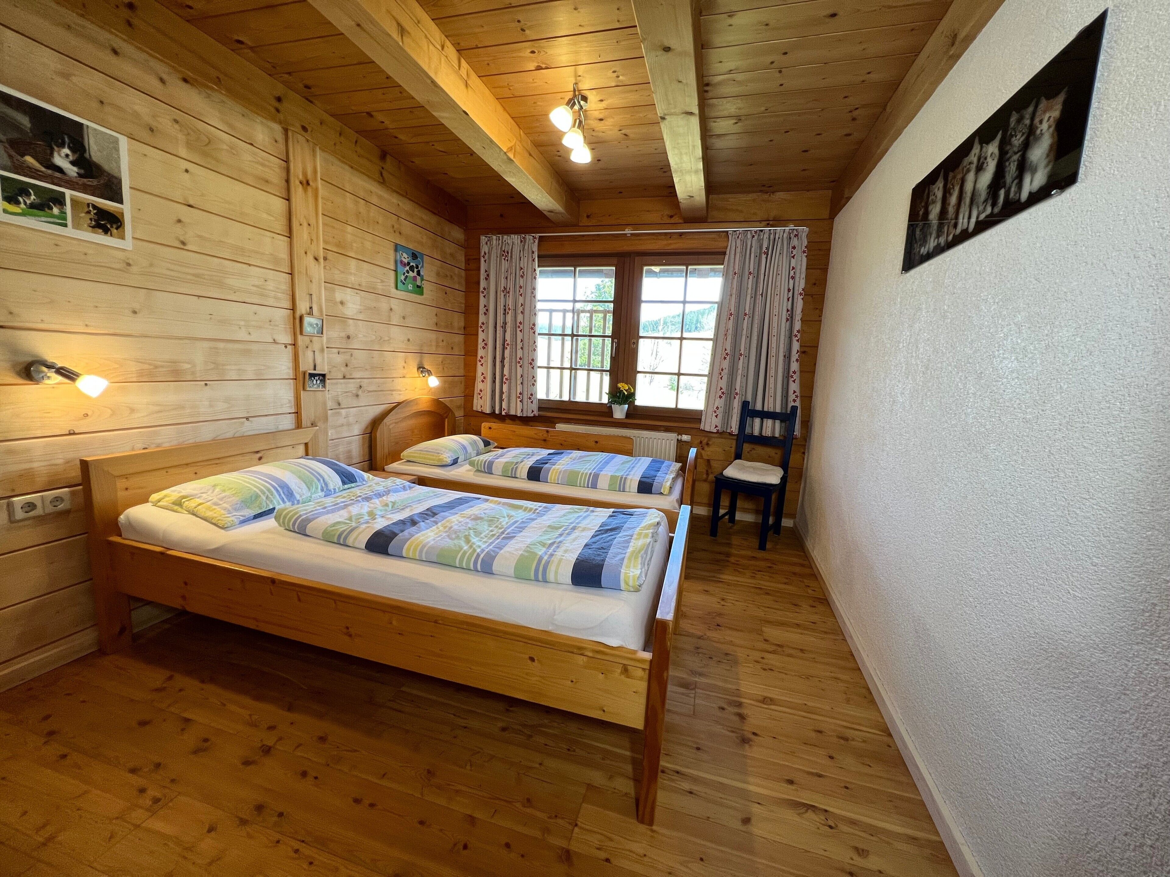 Eine Holzhütte mit zwei Betten, einem Sessel, einem Fenster mit Vorhängen und einem Wandbild.