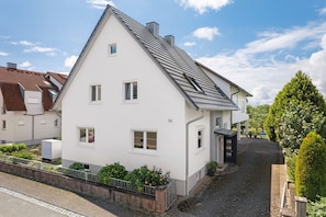 A white two-story house with a sloped roof, a small porch, and a paved driveway.