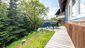 Une terrasse en bois avec une table et des chaises, entourée d’une végétation luxuriante et d’arbres.