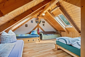Une chambre confortable située dans les combles, avec des poutres en bois, deux lits, une lucarne et un extincteur.