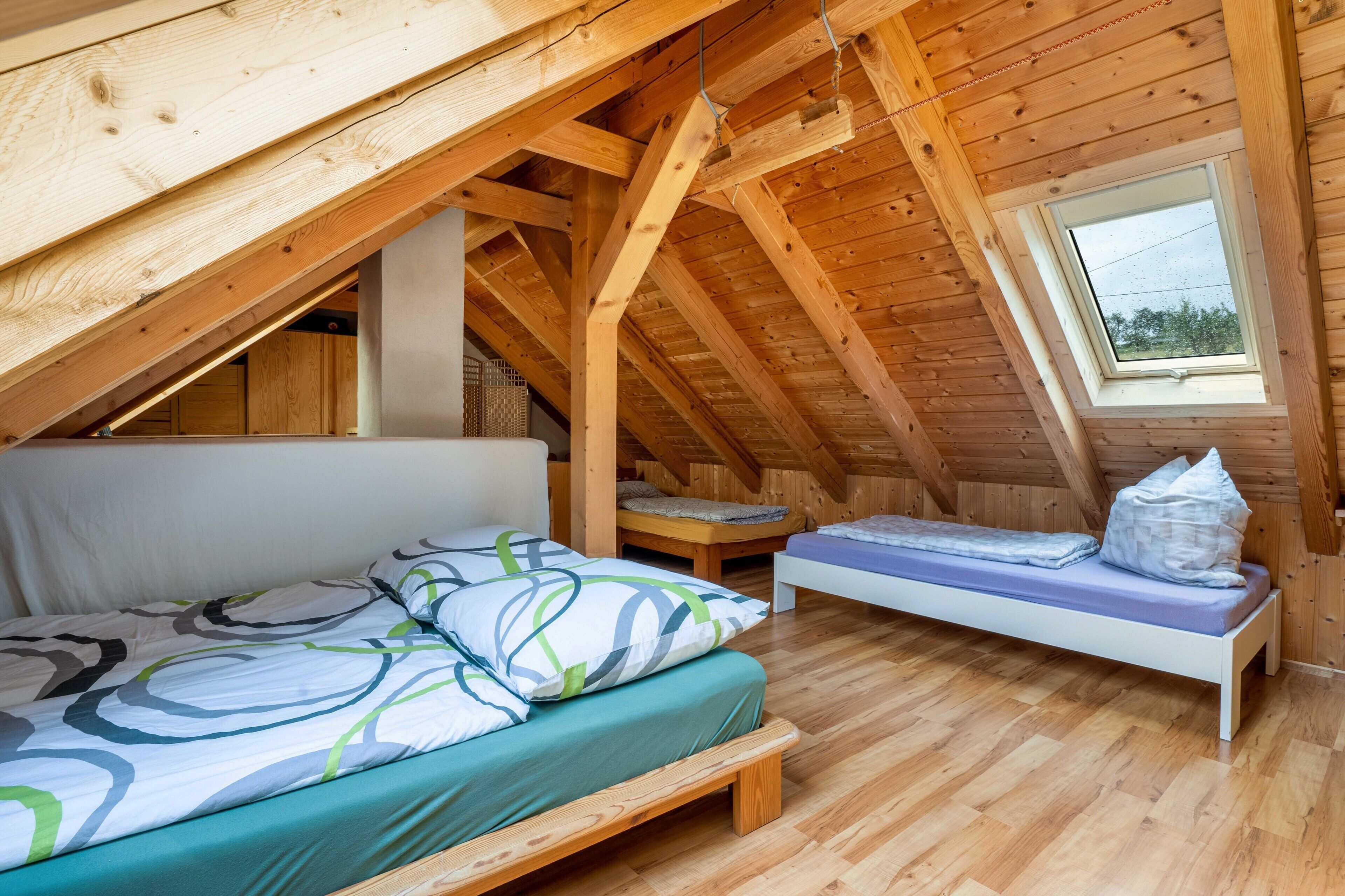 Ein Schlafzimmer im Dachgeschoss mit schrägen Wänden, einem Oberlicht, einem Einzelbett, einer kleinen Bank und Holzboden.
