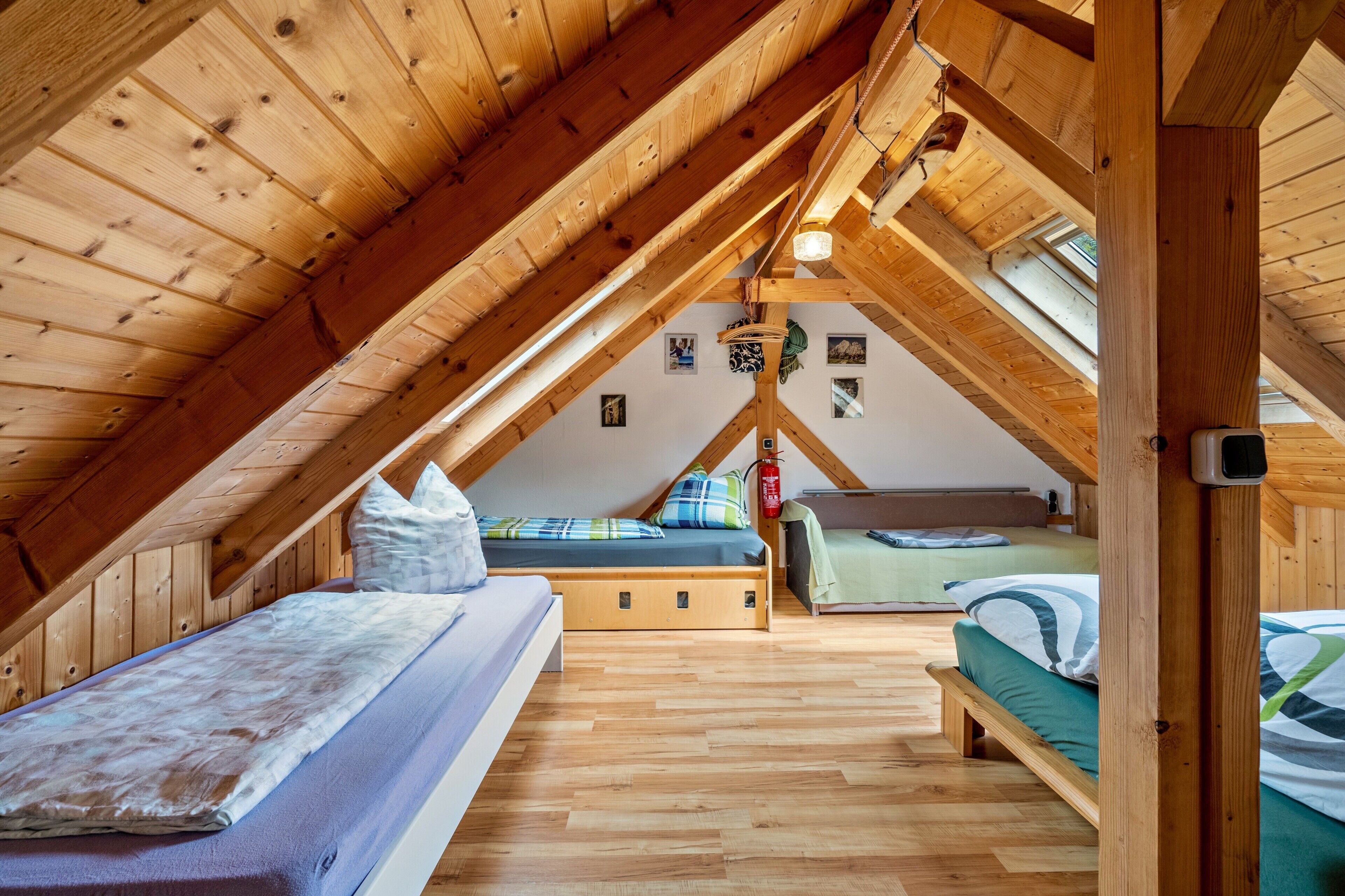 Ein Schlafzimmer im Dachgeschoss mit Holzbalken, einem Etagenbett, einem Einzelbett und einem Dachfenster.