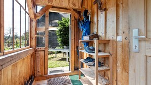 Un intérieur en bois avec une porte coulissante donnant sur un jardin, une étagère à chaussures et un interrupteur sur le mur.