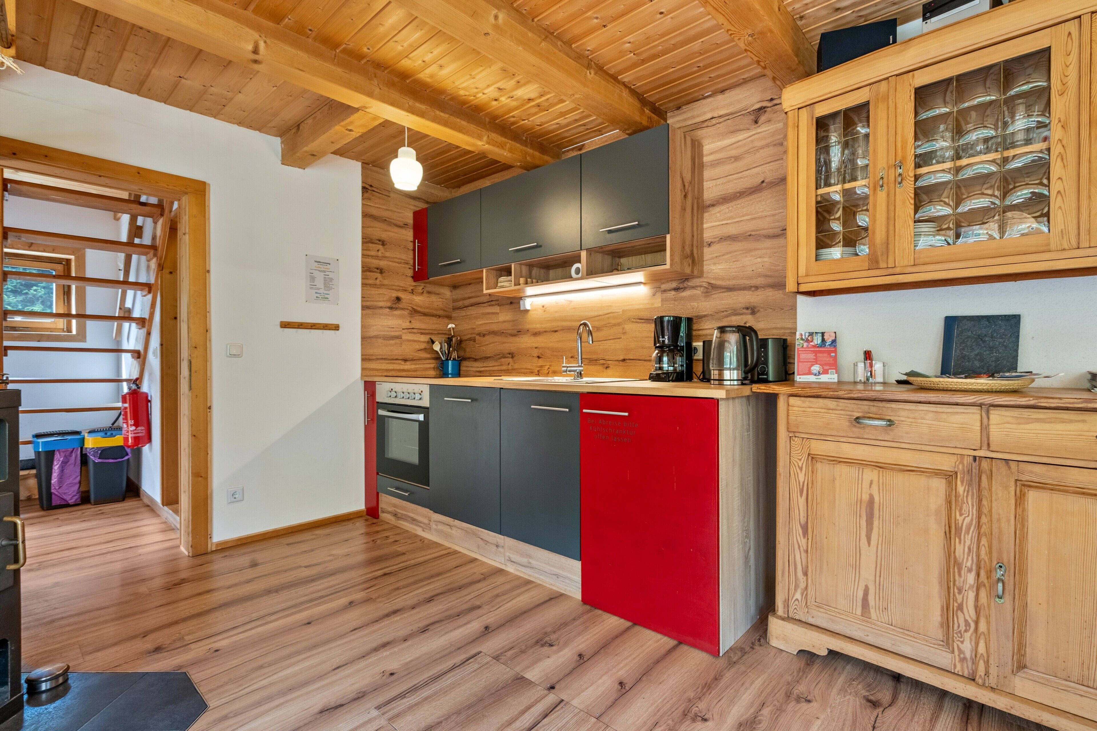 Une cuisine moderne avec des poutres en bois, un meuble rouge et noir, une machine à café et un meuble en bois doté de portes en verre.