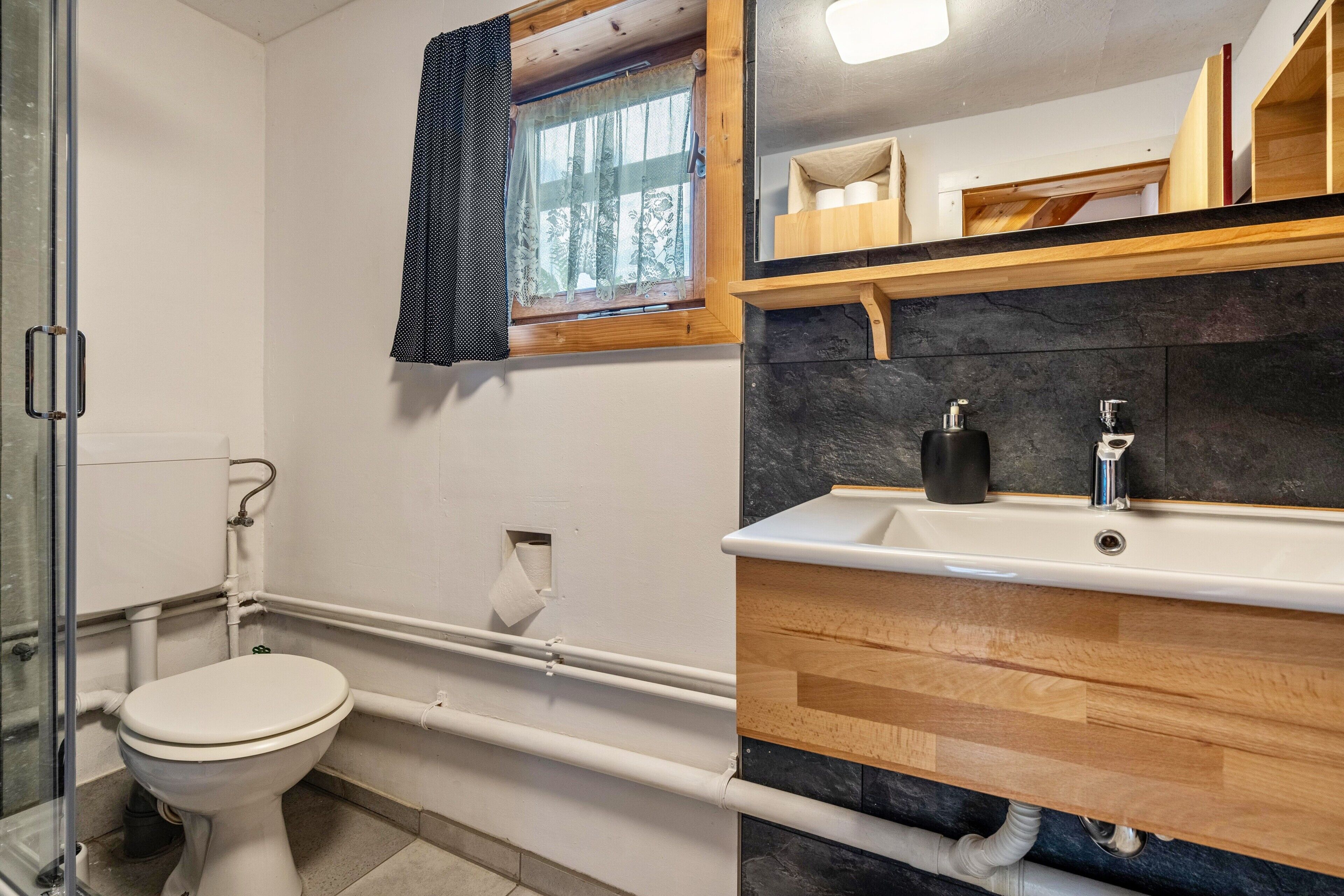 Een badkamer met een toilet, een wastafel, een spiegel en een raam met gordijn.