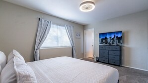 Une chambre à coucher avec un lit, des rideaux, une commode et un tableau représentant un paysage urbain accroché au mur.