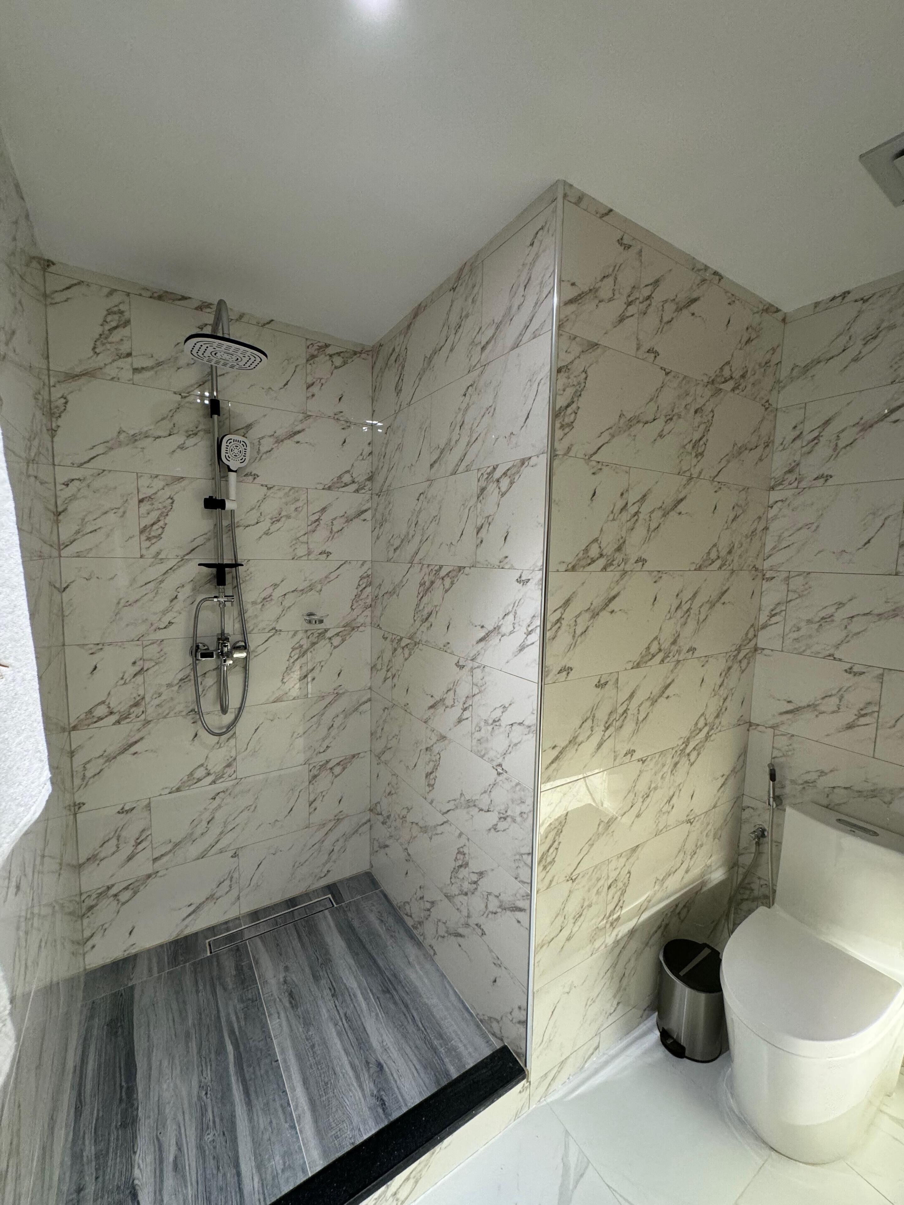 Ein modernes Badezimmer mit Marmorwänden, einer Dusche inklusive Handbrause und einer Toilette.
