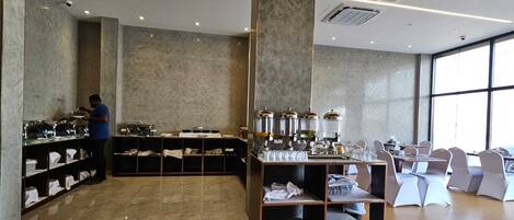 A buffet area with a person serving, a coffee station, and a seating area with chairs.